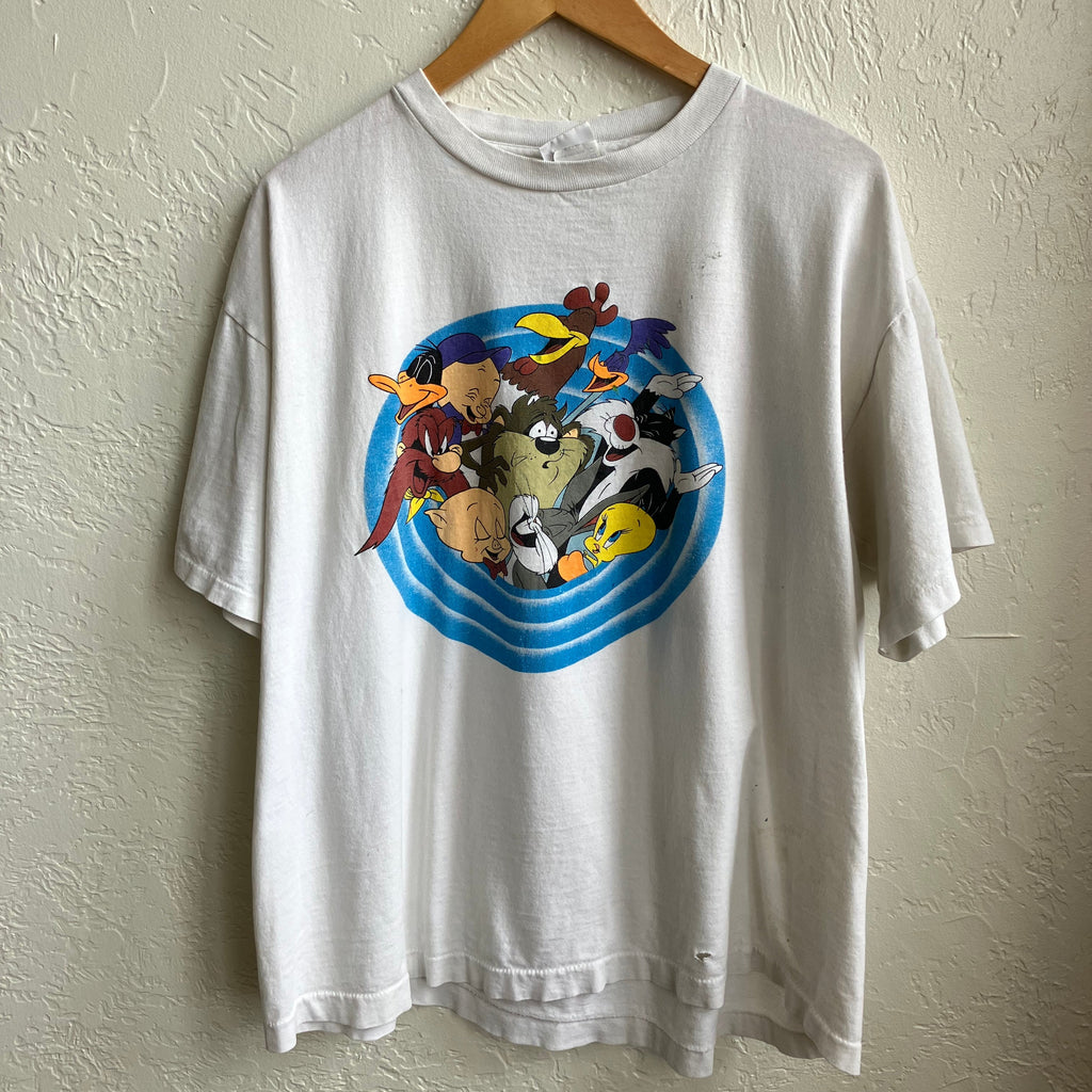 A vintage Looney Tunes themed men's XL T-shirt displayed on a hanger against a white wall, featuring colorful character graphics on the front.