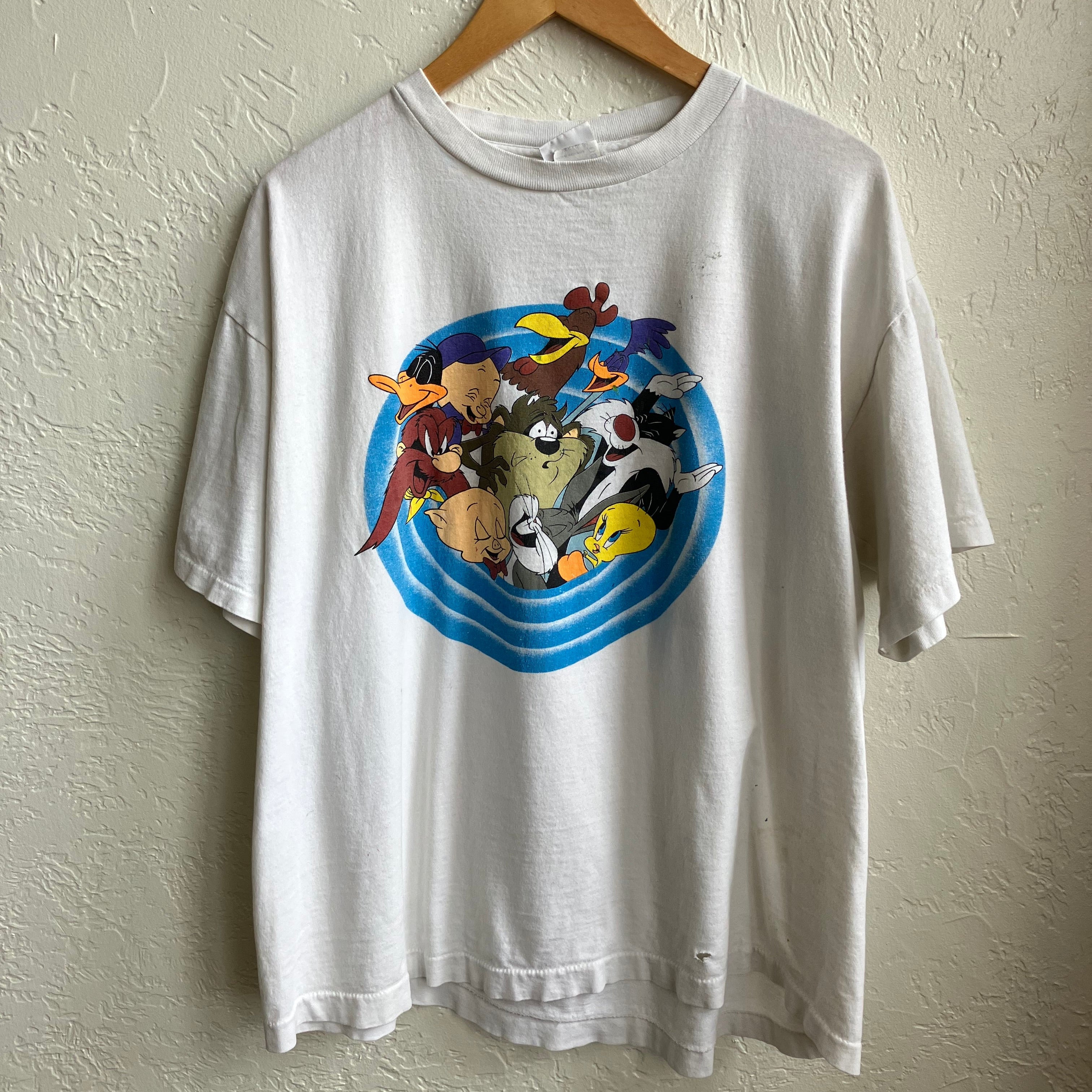 A vintage Looney Tunes themed men's XL T-shirt displayed on a hanger against a white wall, featuring colorful character graphics on the front.